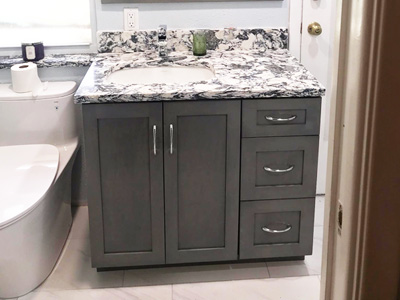 Custom Bathroom Vanity Cabinet with 2 Shaker Doors on Left and 3 Shaker Drawers on Right Side. Shown in Custom Gray/Blue Stain on Maple. Mirror with Frame. Custom Cambria Mayfair Vanity Top, Backsplash, Window Sill and Shower Curb.