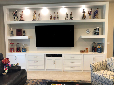 Custom Built-In Mission Shaker Entertainment Center Shown in Solid Bright White on Maple. Custom Modern 10” deep floating shelves with French cleats flank the sides of the TV. 14ft. Long x 9ft High and Accommodates a 75 Inch TV.