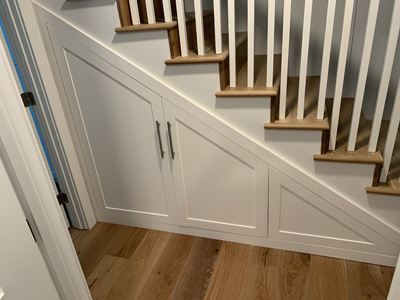 Custom Built-In Under Stairs Hidden Pull-Out Shaker Cabinetry shown in Bright White on Maple