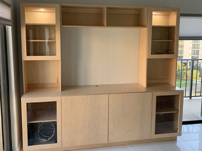 Custom Modern Entertainment Center with Wood Frame Glass Doors and Open Top Center Bridge Cabinet shown in Natural Stain on Maple